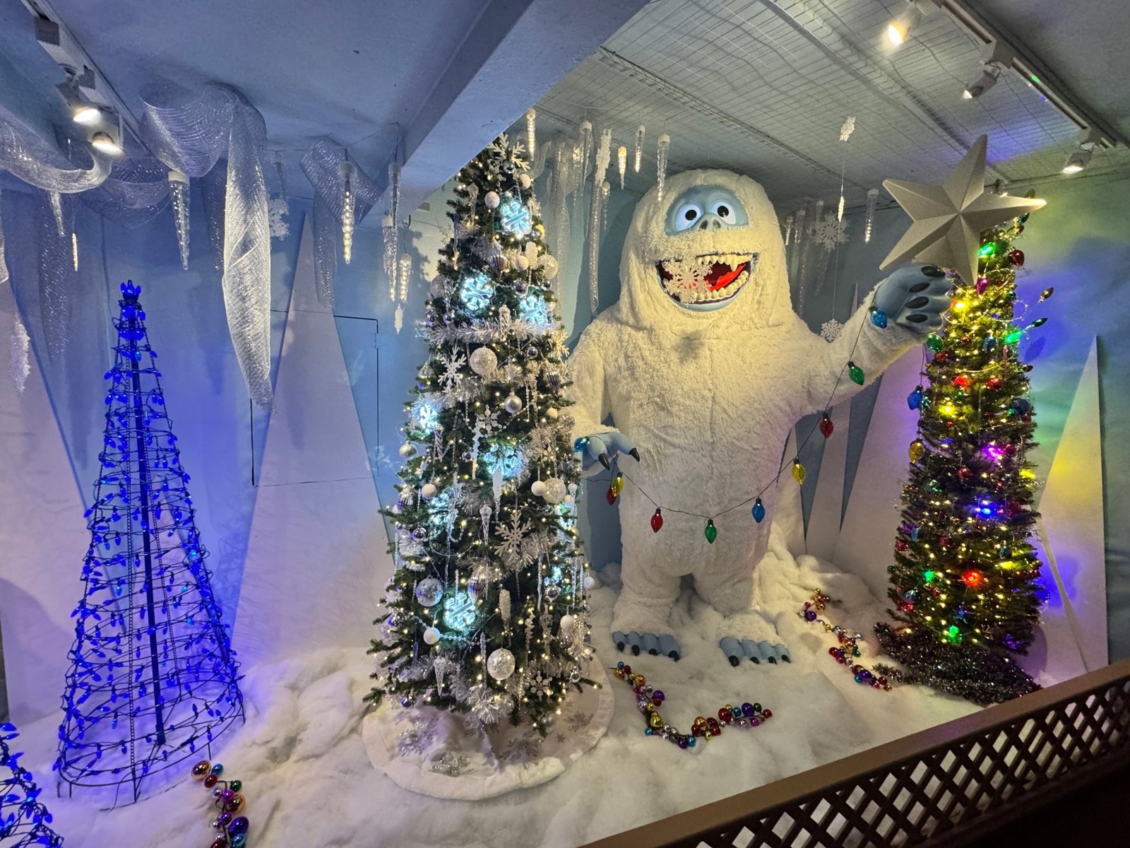 The Bumble abominable snowman holding a string of lights beside decorated trees