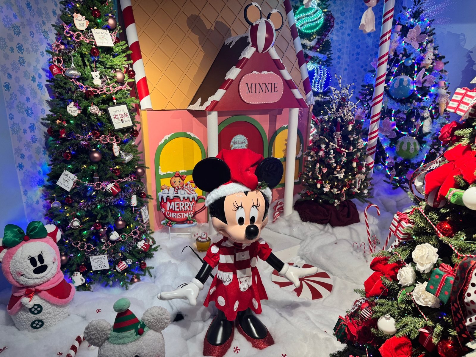 Minnie Mouse in a Santa hat in front of a pink gingerbread house