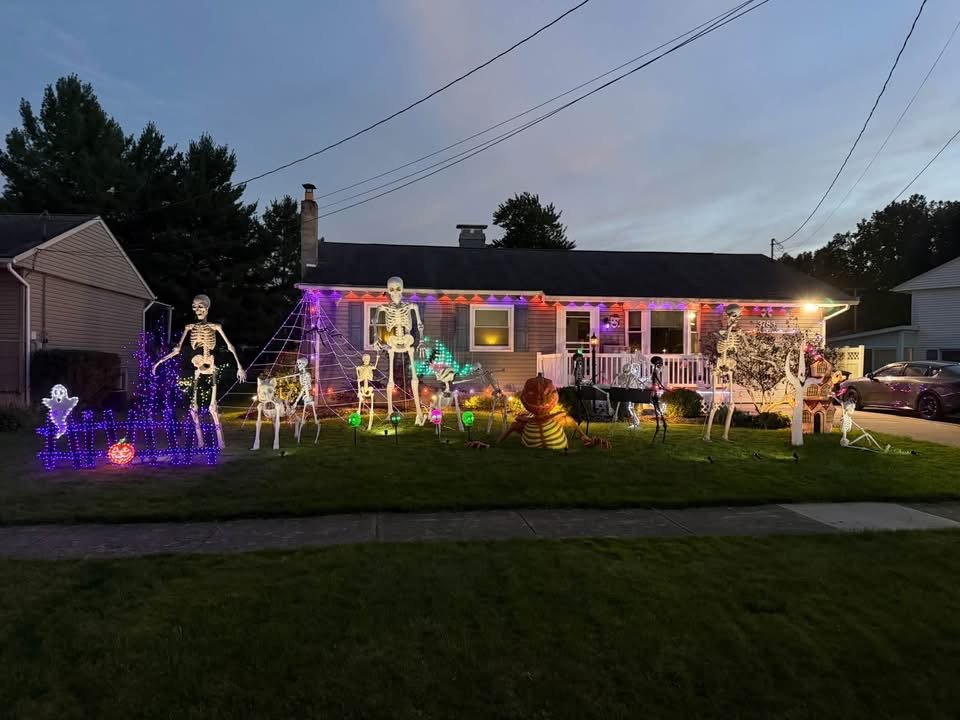 3783 Tod Ave NW in Warren, Ohio, decorated for Halloween with giant skeletons, a glowing teal ghost tree and a purple-lit graveyard fence