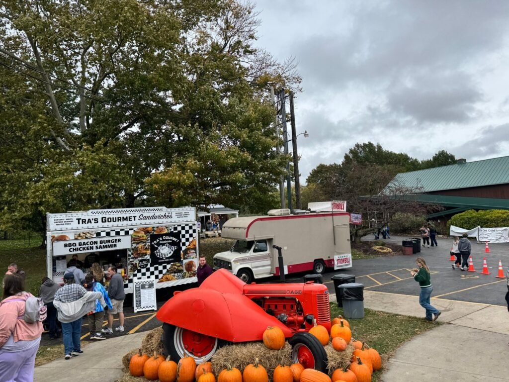Tra's Gourmet Sandwiches food truck and a stromboli truck behind a red Case tractor surrounded by pumpkins